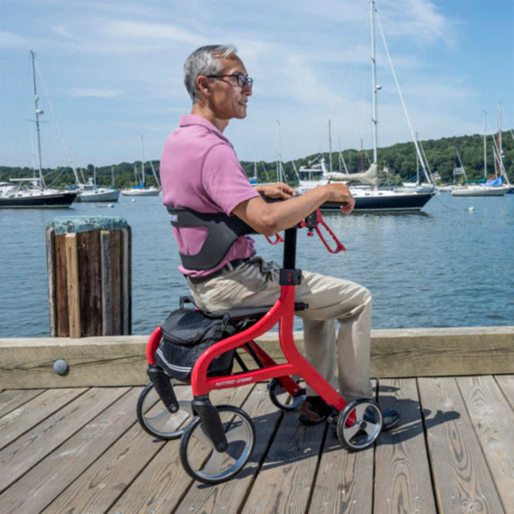 Lifestyle shot of a senior man safely walking along an outdoor paved path using the red Drive Medical Nitro Sprint Rollator.