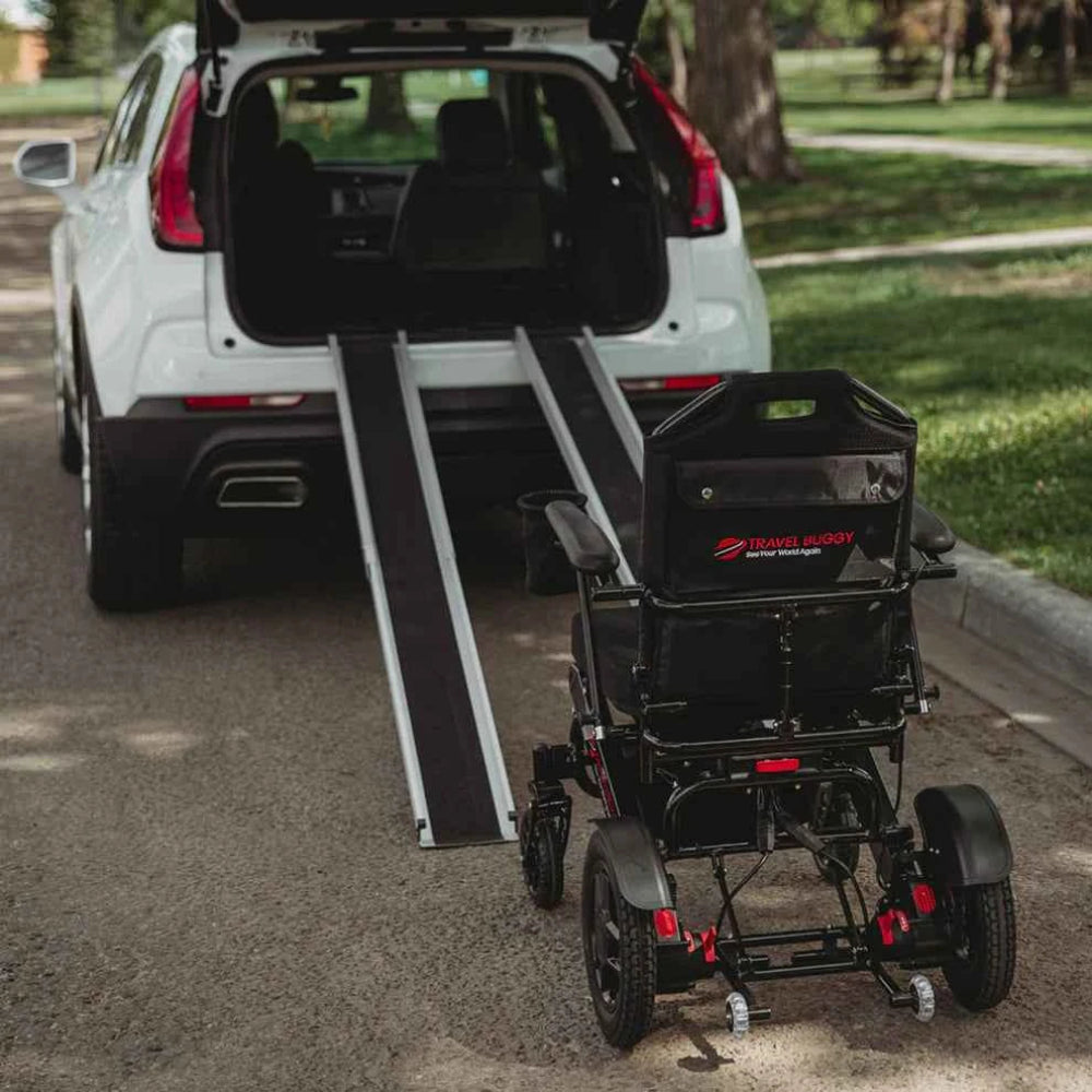 Rear view of a Travel Buggy electric wheelchair being loaded into a vehicle using telescopic portable ramps.