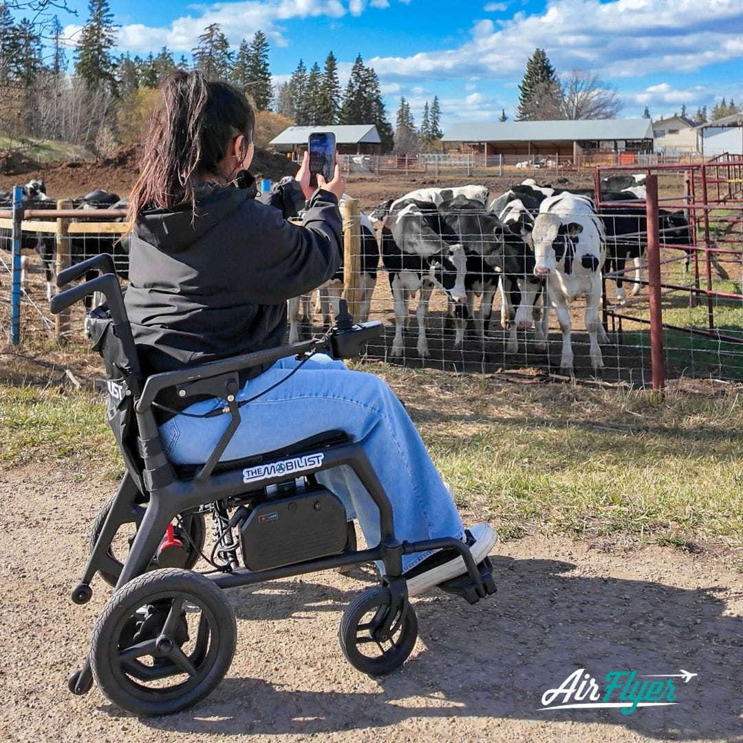 Lifestyle image of a woman confidently driving the AirFlyer power wheelchair along a scenic paved outdoor path.