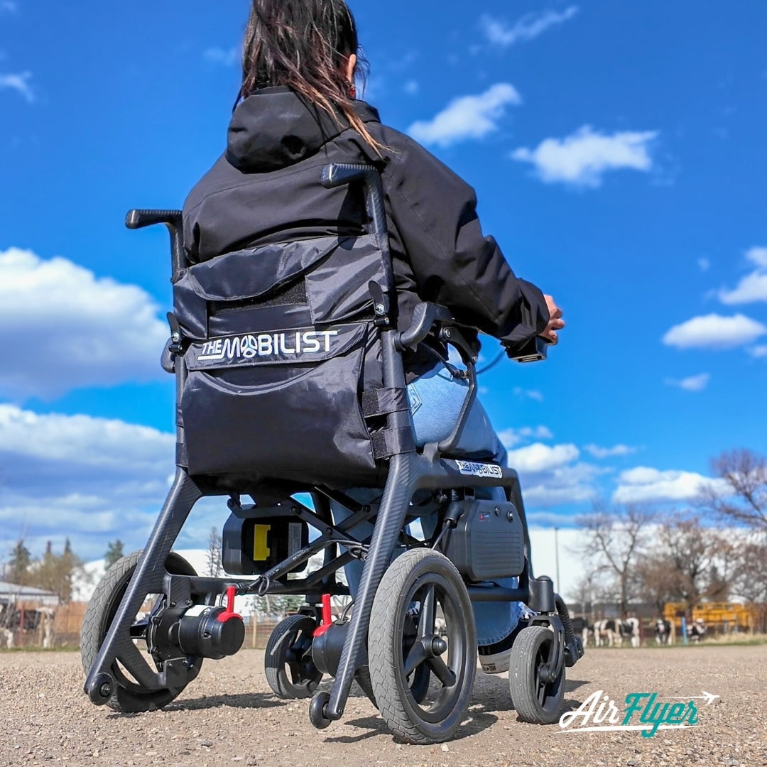 Rear lifestyle view of a woman navigating an outdoor path using the AirFlyer ultra-light electric wheelchair.