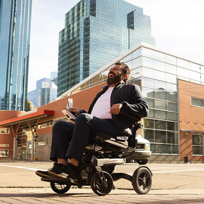 Lifestyle shot of a woman confidently driving the Travel Buggy Grand Tourer GT power wheelchair along a city waterfront.