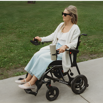 Lifestyle image of a woman confidently driving the AEROLUX power wheelchair along a paved outdoor path.