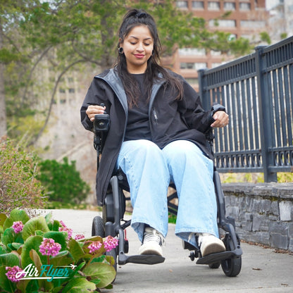Lifestyle shot of a woman smiling and resting comfortably in her AirFlyer carbon fiber electric wheelchair outdoors.