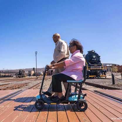 Lifestyle image of a woman relaxing on the Pride Go-Go Super Portable scooter on a wooden boardwalk.
