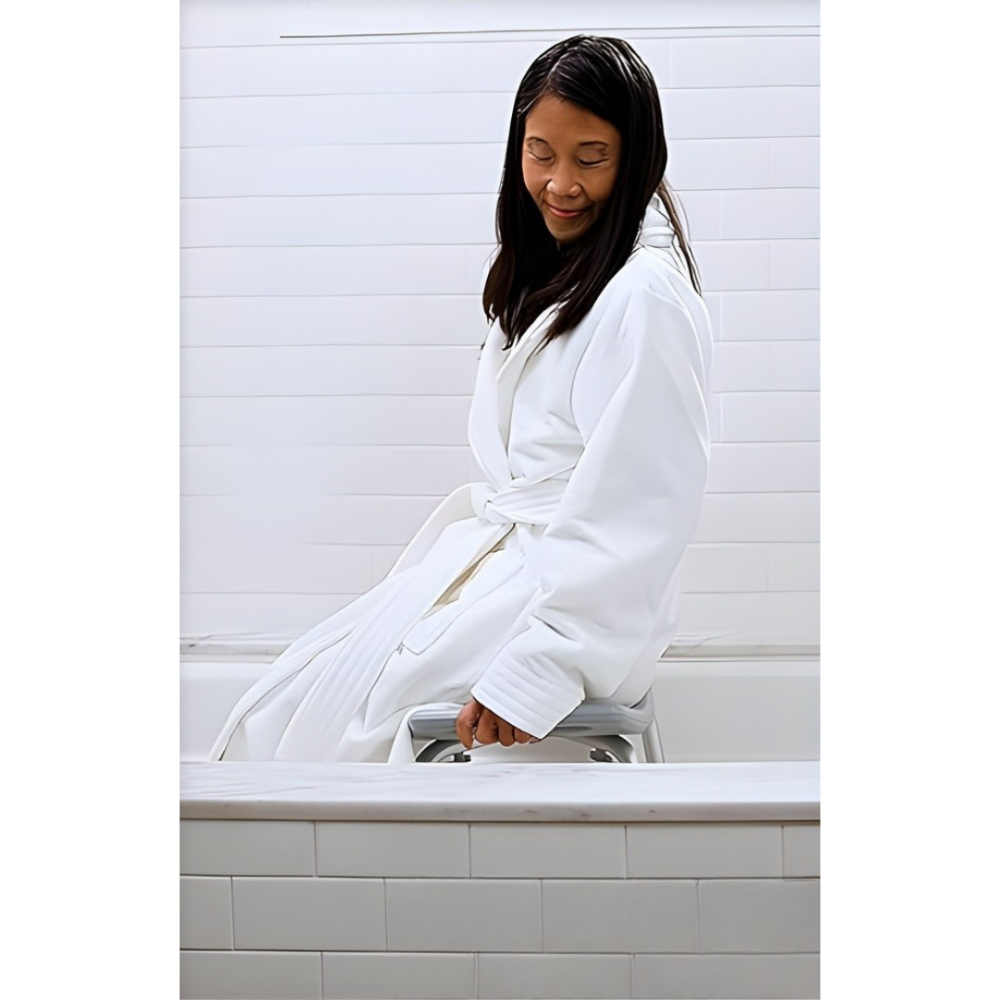 Lifestyle shot of a woman in a white bathrobe safely sitting on the Drive Medical shower bench placed in a standard bathtub.