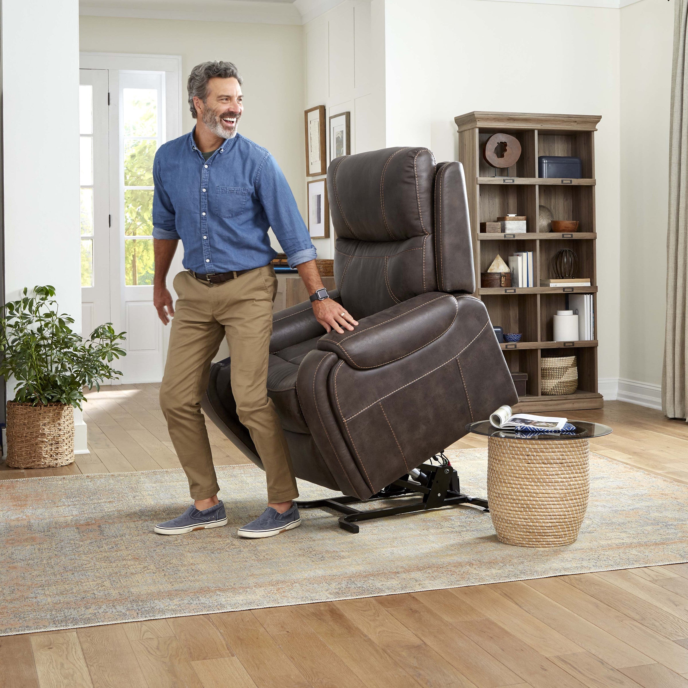 A man standing easily beside the Golden Titan PL449 lift chair with the seat raised to its full lift position in a living room.