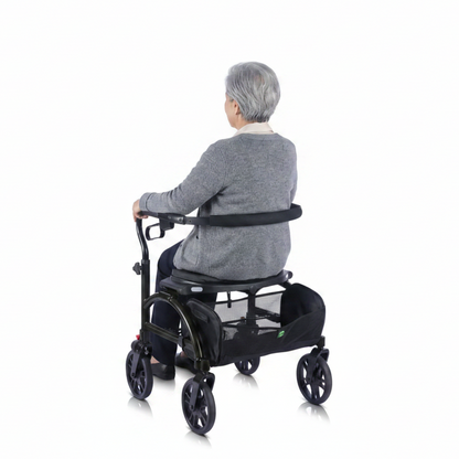 Lifestyle shot of a woman walking outdoors on a paved path from behind, supported safely by the Evolution Xpresso Wide rollator.
