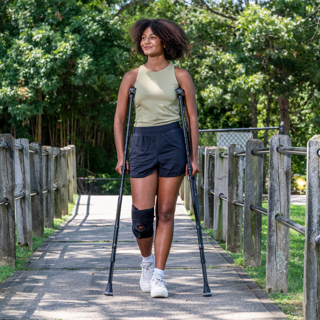 Woman confidently walking outdoors on a paved park path using the black Drive Medical Air-Crutches.